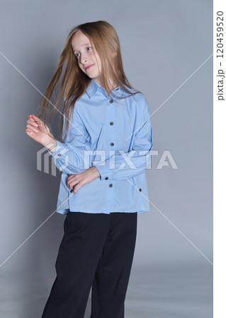 Smiling girl with hands on hips in a blue shirt, exudes confidence. Perfect for themes of youth empowerment and fashion. Smiling girl with hands on hips in a blue shirt, exudes confidence. Perfect for themes of youth empowerment and fashion. 120459520