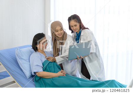 Muslim female doctor using stethoscope checking pressure and young asian female doctor hold laptop and giving advice discussion to elderly patient lie down on bed at hospital. Medicine and health care 120461825