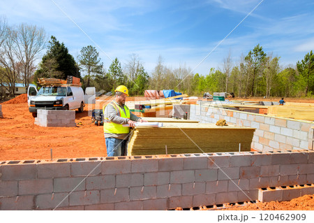 Construction worker in yellow hard hat vest organizes building materials at an active construction supervisor safety vest, hard hat studies blueprints Construction worker in yellow hard hat vest organizes building materials at an active construction supervisor safety vest, hard hat studies blueprints 120462909