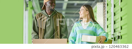 Website header shot of cheerful African American man chatting with girlfriend moving cardboard boxes into self storage unit during apartment decluttering 120463362