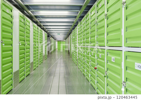 Background image of aisle with green metal doors closed on locks leading to self storage units at warehouse, copy space 120463445