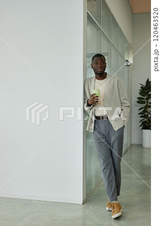 Vertical shot of African American businessman wearing beige smart casual outfit for office captured during coffee break standing next to wall in coworking, copy space 120463520