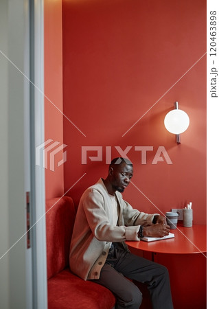 Vertical shot of concentrated African American businesswoman writing in notebook planning working schedule ahead while sitting at cafe table with colorful minimalistic design, copy space Vertical shot of concentrated African American businesswoman writing in notebook planning working schedule ahead while sitting at cafe table with colorful minimalistic design, copy space 120463898