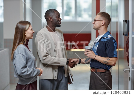 Medium shot of African American male boss giving motivational handshake to positive employee making business deal while standing in modern office building Medium shot of African American male boss giving motivational handshake to positive employee making business deal while standing in modern office building 120463921