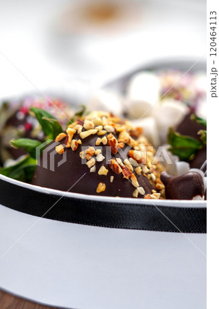 Chocolate covered strawberries with crushed nuts and marshmallows in decorative paper cups of sweet gift kit. Fresh green berry leaves. Macro shot Chocolate covered strawberries with crushed nuts and marshmallows in decorative paper cups of sweet gift kit. Fresh green berry leaves. Macro shot 120464113