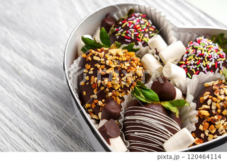 Handmade strawberry dessert coated in crushed nuts and white glaze in paper container. Fresh green leaves add a vibrant touch. Styled for festive look Handmade strawberry dessert coated in crushed nuts and white glaze in paper container. Fresh green leaves add a vibrant touch. Styled for festive look 120464114
