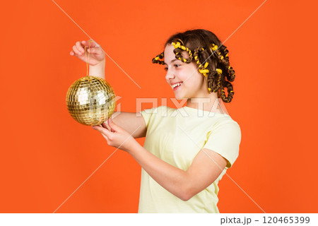 Hairstyle for disco party. Have fun. Retro party. Child hold golden disco ball. Cheerful girl with disco ball. Fashion kid posing with curlers in hair. Night club. Hairdresser salon. Fancy teen 120465399