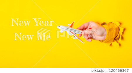Hand holding a toy airplane with the words New Year Now Me written below it 120466367