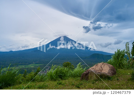 A viewpoint with a large stone and a view of the sacred volcano Agung covered with clouds on a rainy day on the island of Bali. View of the mountain. 120467379