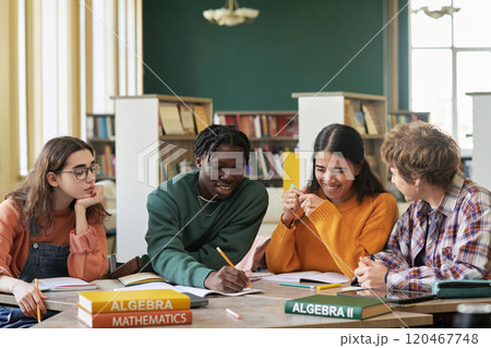 Group of high school students sitting at a table in bright library, engaging in a study session. Various textbooks on math subjects spread across table Group of high school students sitting at a table in bright library, engaging in a study session. Various textbooks on math subjects spread across table 120467748