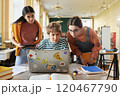 Three young professionals collaborating using laptop in bright, modern office. Diverse group engaging in discussion, sharing ideas, and planning project without eye contact with camera 120467790