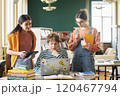 Three female students discussing study materials in library with books and laptop on table while engaging in collaborative learning session 120467794