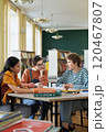 Group of young students sitting around a table in a library, engaging in collaborative study session with books and notebooks. Bright light fills the room, enhancing the studious atmosphere 120467807