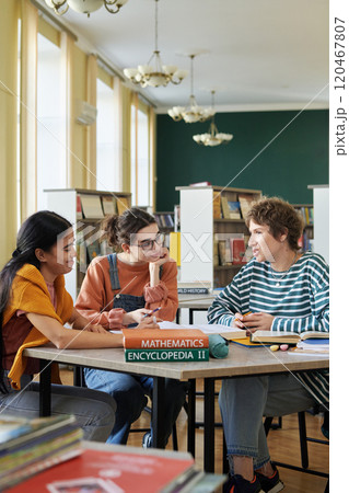 Group of young students sitting around a table in a library, engaging in collaborative study session with books and notebooks. Bright light fills the room, enhancing the studious atmosphere Group of young students sitting around a table in a library, engaging in collaborative study session with books and notebooks. Bright light fills the room, enhancing the studious atmosphere 120467807