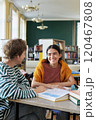 Two smiling students studying at library table surrounded by books amidst sunlight streaming through windows 120467808