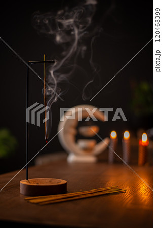 An incense stick burning and generating aromatic smoke surrounded by small candles 120468399