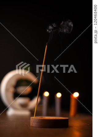 An incense stick burning and generating aromatic smoke surrounded by small candles An incense stick burning and generating aromatic smoke surrounded by small candles 120468400