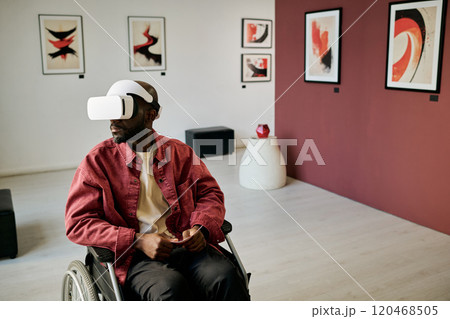 Man in wheelchair exploring modern art gallery using virtual reality headset with abstract paintings on walls and contemporary decor elements surrounding him Man in wheelchair exploring modern art gallery using virtual reality headset with abstract paintings on walls and contemporary decor elements surrounding him 120468505