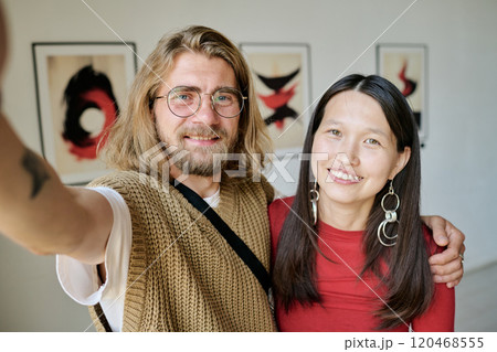 Smiling close friends capturing moment with artwork in background using smartphone creating lasting memories looking at camera Smiling close friends capturing moment with artwork in background using smartphone creating lasting memories looking at camera 120468555