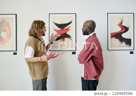 Two men talking and analyzing abstract artwork in modern gallery setting. They are paying close attention to the details and discussing perspective techniques 120468566