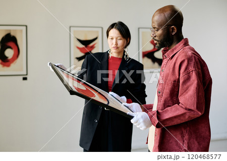Two individuals intently examining modern art pieces in a gallery setting with a focus on abstract paintings and captured during an engaging discussion Two individuals intently examining modern art pieces in a gallery setting with a focus on abstract paintings and captured during an engaging discussion 120468577