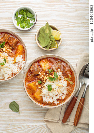 Two bowls of delicious massaman curry with beef, potatoes, rice, and peanuts, garnished with parsley on white wooden background, Thai cuisine 120468662
