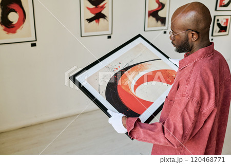 Bearded Black person examining abstract painting in art gallery holding artwork in hand Bearded Black person examining abstract painting in art gallery holding artwork in hand 120468771