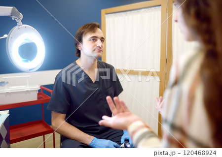Portrait of a doctor. A caring dermatologist examines a female patient during an appointment. A young woman talks about her symptoms. Portrait of a doctor. A caring dermatologist examines a female patient during an appointment. A young woman talks about her symptoms. 120468924