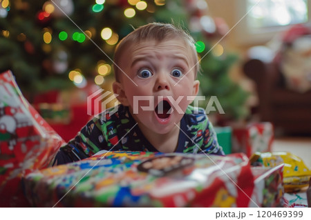 Surprised toddler opening Christmas presents under the Christmas tree with a shocked expression 120469399