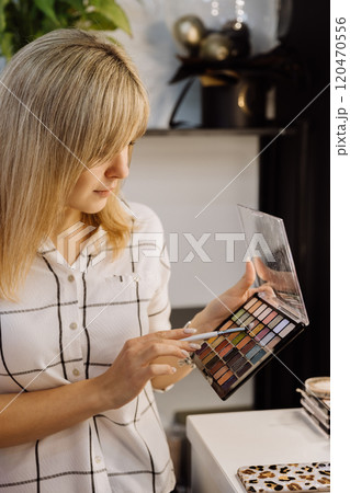 Focused woman choosing colors from a vibrant eyeshadow palette for professional makeup application 120470556