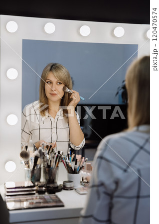 Applying makeup with a brush in front of a lighted mirror for a professional look Applying makeup with a brush in front of a lighted mirror for a professional look 120470574