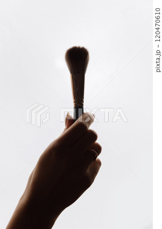 Silhouette of a hand holding a makeup brush against a white background, minimalist beauty concept Silhouette of a hand holding a makeup brush against a white background, minimalist beauty concept 120470610
