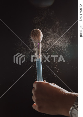 Powder brush in dramatic lighting with floating particles, beauty and makeup artistry in action 120470612