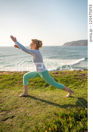 Mature woman practicing warrior pose on grassy Mature woman practicing warrior pose on grassy 120470858