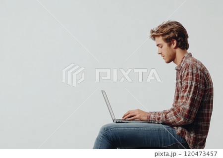 A man is sitting on a chair and typing on a laptop 120473457
