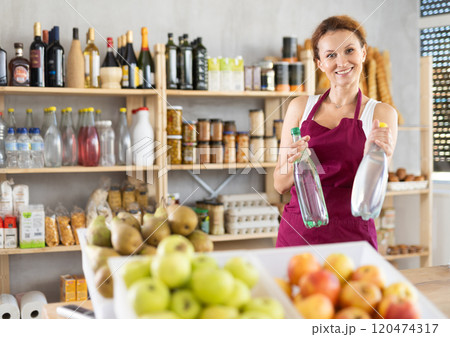 Adult woman seller offers water in grocery store Adult woman seller offers water in grocery store 120474317