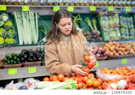 Young female shopper selects and buys tomatoes in supermarket Young female shopper selects and buys tomatoes in supermarket 120474320