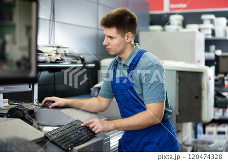 Man in uniform operating computerised machne to mix paint 120474328