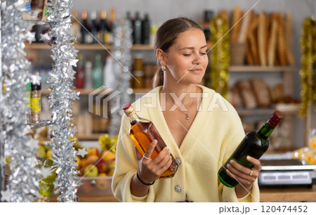 On New Years Eve, girl shopper compare wine and whisky, buys alcoholic beverages 120474452