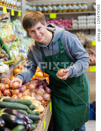 Young salesman lays out onions on counter Young salesman lays out onions on counter 120474568