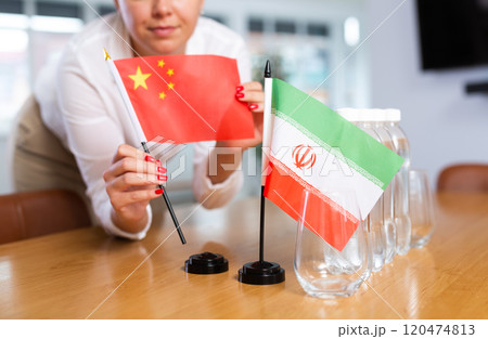 Little flag of Iran on table and flag of China put next to it by young woman Little flag of Iran on table and flag of China put next to it by young woman 120474813