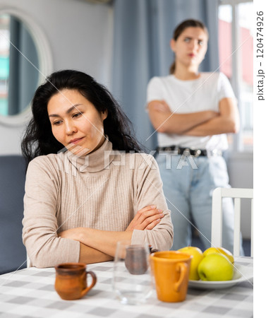Woman sitting at table at home while having quarrel with her friend Woman sitting at table at home while having quarrel with her friend 120474926