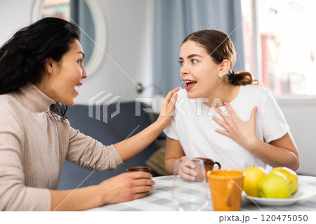 Smiling woman with cup of tea talking with girlfriend at home 120475050