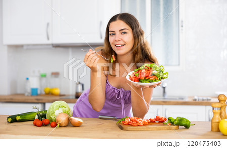 Smiling young woman eating salad at home 120475403