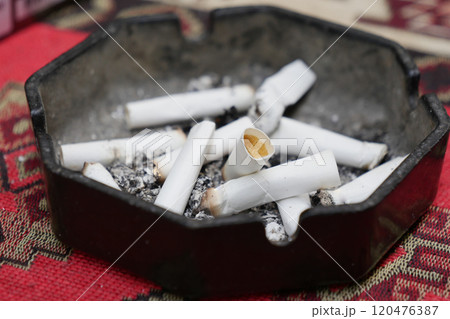 An ashtray filled with scattered cigarette butts and ashes from regular use over time 120476387