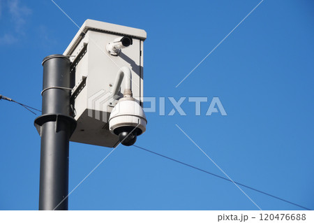 A surveillance camera is firmly mounted on a pole, set against a clear blue sky backdrop 120476688
