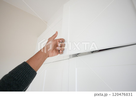 A person is reaching for the upper cabinet door in a beautifully designed modern kitchen space 120476831