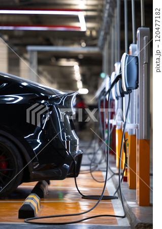 EV charger and electric car, Electric car charger station for charge ev battery, Plug for vehicle with electric engine, EV charger clean energy, Charging point at car parking lot department store. 120477182