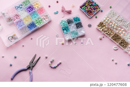 Crafting beautiful jewelry with beads and supplies on a pastel pink surface Crafting beautiful jewelry with beads and supplies on a pastel pink surface 120477608