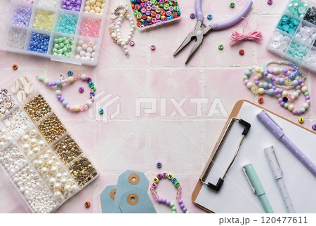 Colorful beads and jewelry making supplies arranged on pink tile background with clipboard and pens 120477611